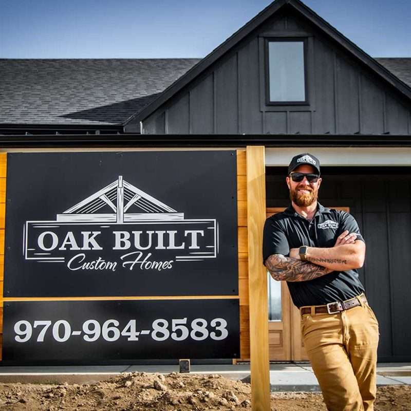 Charlie Mezzenga of Oak Built Custom Homes standing near a sign sporting their logo and phone number
